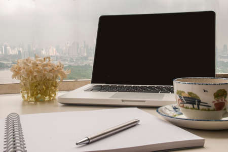 Working corner on the balcony with a laptop, notebook, pen, coffee and flowers overlooking the riverの写真素材