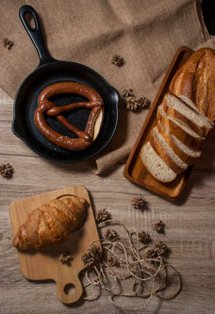 Croissants and fresh pretzels with baguette bread, placed on a tray and a wooden chopping board, placed on a wooden table from the top view.の写真素材