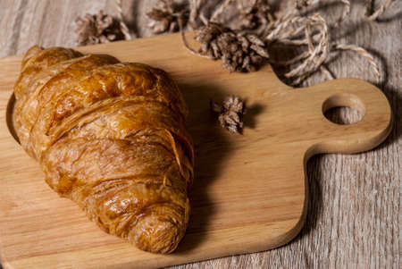 Fresh croissants placed on a wooden cutting board on a wooden table ready to eatの写真素材