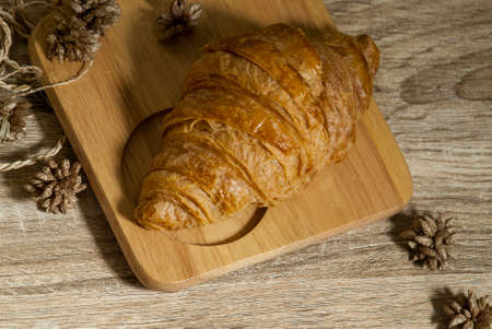 Fresh croissants placed on a wooden cutting board on a wooden table ready to eat from the top viewの写真素材