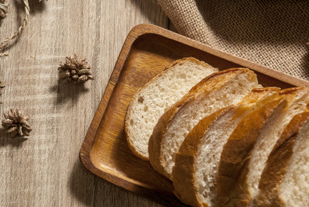 Baguette on a wooden tray placed on a sackcloth on a wooden table to serve from the top view.