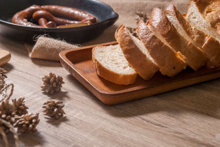 Baguette is fresh on a wooden tray and pretzel on a black bowl, placed on a wooden table for service.の写真素材