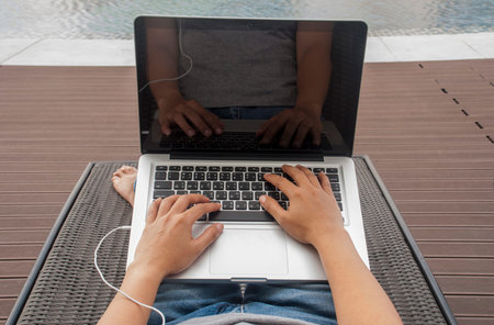 The hands of women who are printing on a poolside laptop on holiday