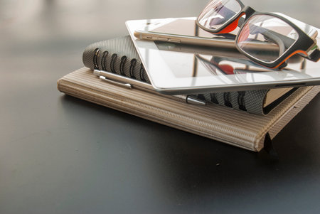 Camera, glasses, mobile phones, car keys, pens, and 2 notebooks, placed on a black table