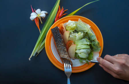 Grilled salmon steak served with vegetable salad on a black tableの写真素材
