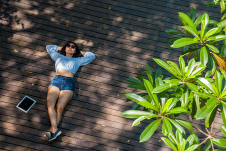 The blue shirt woman is sitting watching the text on the tablet while sitting in the park from a high angle.の写真素材