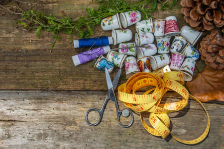 Spools of thread and basic sewing tools including pins, needle, a thimble, and tape measure on an old wooden tabletop. concept with copy space.の写真素材