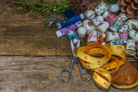 Spools of thread and basic sewing tools including pins, needle, a thimble, and tape measure on an old wooden tabletop. concept with copy space.の写真素材