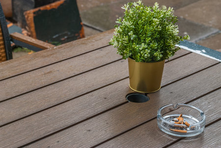 Glass ashtray and cigarette butts are extinguished on the wooden table, Oblique view from the top.