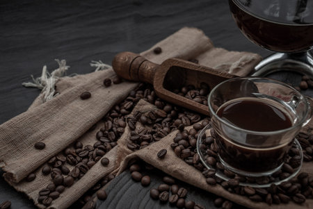 Coffee style, Cup of coffee and coffee beans roating with old wooden scoop and coffee beans around on the wooden and dark stone background. Oblique view from the top with copy space for your text.の写真素材