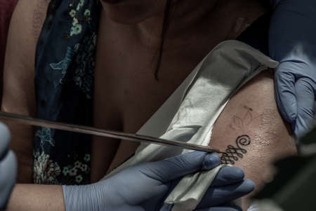 Bangkok, Thailand - 25 Aug 2019 : Tattooing Thai style concepts. Tattoo artist creating a tattoo on a girl's arm with a pointed metal.のeditorial素材