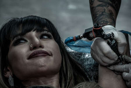 Bangkok, Thailand - 25 Aug 2019 : Tattooist making by professional artist is tattooing body sexy woman using machine in a creative design work studio. Process decoration ink artwork female skin pattern.のeditorial素材