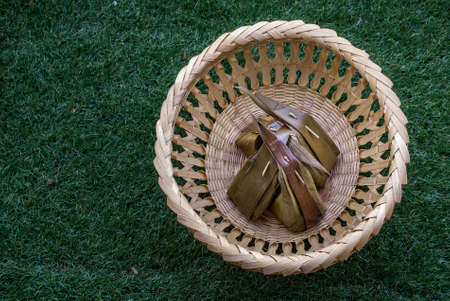 Thai dessert steamed flour with coconut filling stuffed in banana leaf (Kanom Sai Sai) and coconut leaf on basket, Thai Traditional Dessert, Top view. copy space.の写真素材