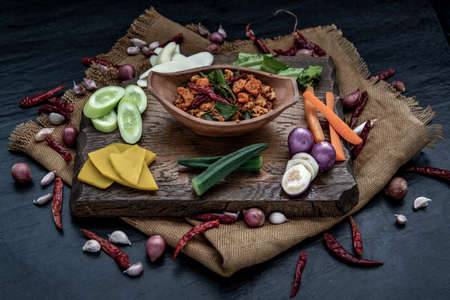 Pork Crackling Chili Paste with fried kaffir lime leaves with the ingredient and fresh vegetables on wood background, Oblique view from the top.の写真素材