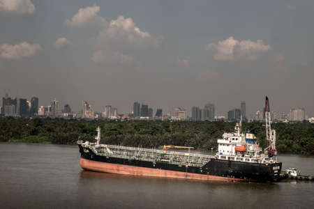 Bangkok, Thailand - 24 Oct 2019 : A cargo ship parked in the middle of the river and in front of a green tree by the Chao Phraya River.のeditorial素材