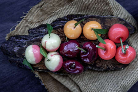 Close-up of Kanom Look Choup : An old traditional thai dessert made from green been, coconut milk, sugar and jelly, Deletable imitation fruits made from green been, coconut milk, sugar and jelly in fruit shape on wooden, It is a unique dessert of Thailand, Top view.の写真素材