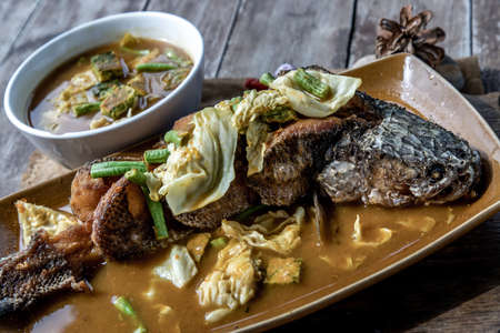 Deep fried whole Snakehad fish topped with Acacia omelets in vegetable sour soup (Orange curry with Cha-om).の写真素材