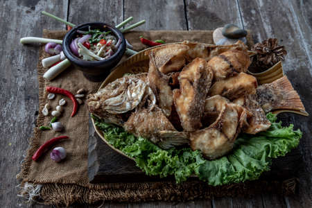Deep fried Tubtim fish with fish sauce on vintage wooden, The perfect frying process, Set hot fire, then bring the Tubtim fish to fry to frame and topped with fish sauce.の写真素材