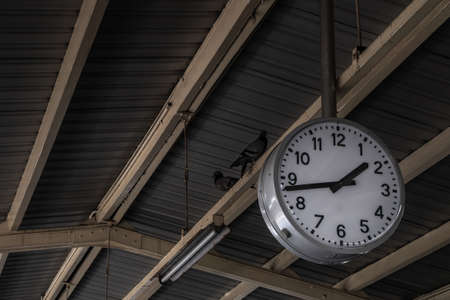 Clock or watch attach the pole under the roof, Beautiful big white clock or watch with line numbers is hanging under the roof of train station.の写真素材