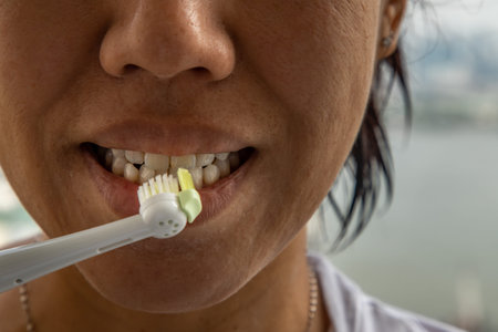 Closeup on young woman brushing teeth with Electric toothbrush on white background.