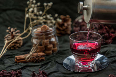 Roselle tea (Jamaica sorrel, Rozelle or hibiscus sabdariffa ) is poured from a kettle into glass cup  with dry roselle and brown cane sugar cube. Healthy herbal tea rich in vitamin C and minerals. The concept of health. Organic and Summer drink, Drinks & Beverages, Selective Focus.の写真素材