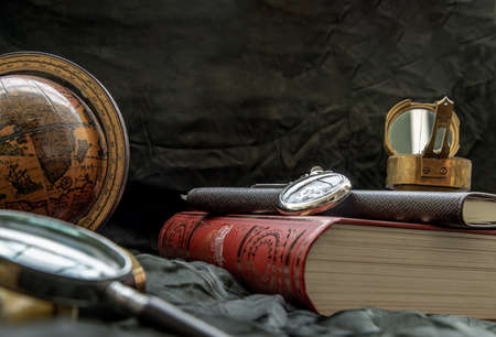 Travel or adventure concept background. Pocket watch, binoculars, antique compass, globe, magnifying glass and stack of books on dark background. Journey Concept, Vintage Style.の写真素材