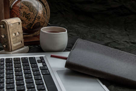 Workplace side view with laptop screen, keyboard, globe, desktop calendar, coffee mug and notebook with pencil at office workplace. Creative concept. Blogger's decorated workspace. Space for text, Selective focus.の写真素材