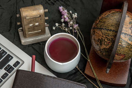 Workplace side view with laptop screen, keyboard, globe, desktop calendar, flower, fruit juice mug and notebook with pencil at office workplace. Creative concept. Blogger's decorated workspace. Selective focus.の写真素材