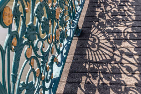 Wrought iron decorative fence on bridge. Forming an interesting design with it's cast shadow on the floor. Selective focus.の写真素材