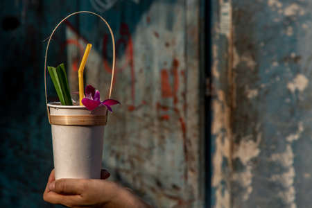 Pandan juice and orchids in a paper cup in a woman hand with blurred background. Natural herbal plant and healthy drinks concept. Selective focus.の写真素材