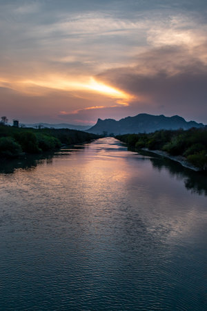 A view of the beautiful during the evening of the lake as the sun sets behind the hills and adds a...