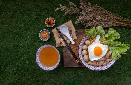 Boil egg noodles with pork ball, minced pork, fried egg, vegetables and soups in bowl and chopstick with spoon and timber background. Thai noodle soup.の写真素材
