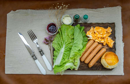 Continental breakfast with scrambled eggs, fried sausages, vegetable and scones served with cmascarpone cheese and raspberry jam on  Wooden background, Selective focuse.の写真素材