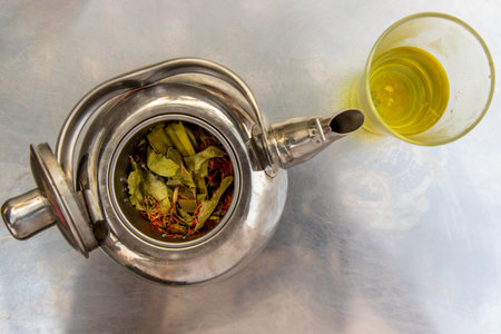 Teapot herbal with glass of hot herbal tea on a stainless steel table, Top view
