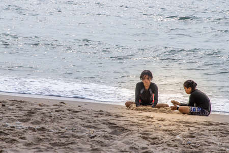 Phetchaburi,Thailand - Mar 15, 2020 : Two girls playing sand on the tropical beach on a sunny day. Vacation trip. Selective focus.のeditorial素材