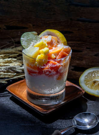 Tropical fresh fruit salad with milk and oatmeal in a glass cup on dark background. Sweet healthy breakfast, Healthy vegan meal. Selective focus.の写真素材
