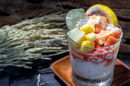 Tropical fresh fruit salad with milk and oatmeal  in a glass cup on dark background. Sweet healthy breakfast, Healthy vegan meal. Selective focus.の写真素材