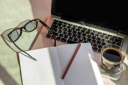 Closeup shot of Workspace with laptop, sunglasses, a glass of coffee notebook and pencils. Remote working concept or Business workspace.の写真素材
