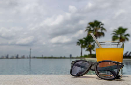 Relaxing moment by the pool. Take a break from enjoy the fresh orange juice for a refreshment. Outdoor swimming pool background. leisure activity.の写真素材