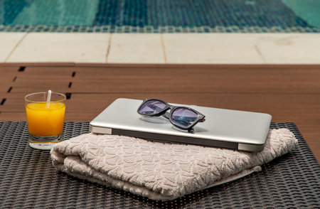Relaxing moment by the pool. Take a break from working on laptop and enjoy the fresh orange juice for a refreshment.  Outdoor swimming pool background. leisure activity.の写真素材