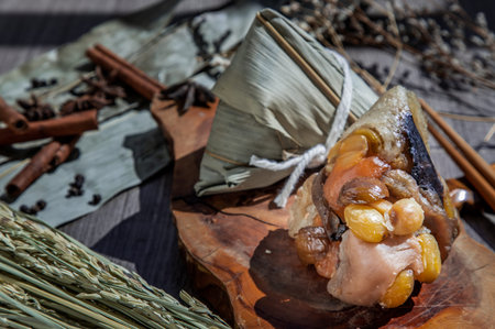 Chinese rice dumpling (Zongzi) shaped pyramidal wrapped by leaves ingredients on wooden plate and...