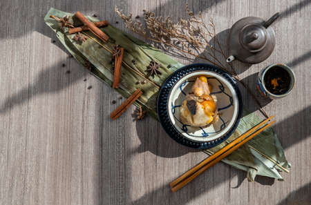 Chinese rice dumplings (Zongzi) shaped pyramidal wrapped by leaves ingredients on bowl chinese style and chopsticks served with chinese tea. Famous asian tasty handmade food in dragon boat (duan wu) festival occasion.の写真素材
