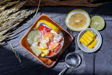 Tropical fresh fruit salad with milk and oatmeal in a glass cup served with corn on dark background. Sweet healthy breakfast, Healthy vegan meal. Top view, Selective focus.の写真素材