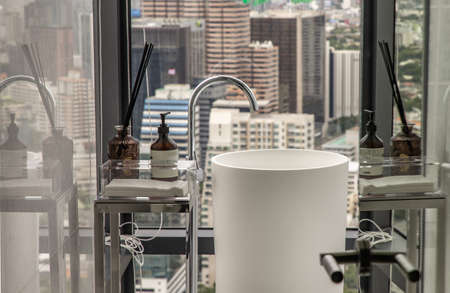 Modern white restroom with cityscape that can look outside from big window. Elegant faucets and components, Sanitary ware, The concept of health care. Selective focus.の写真素材