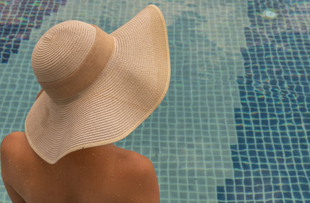Short haired young woman relax sitting on the edge of roof top outdoor swimming pool and enjoying...