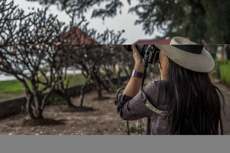 Young woman wearing a white hat and taking a camera to take pictures of the scenery on the sea...