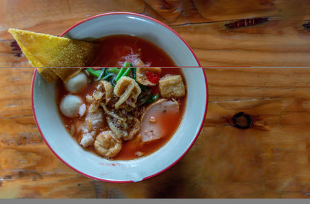 Yentafo Thai Noodle with pink soup in ceramic bowl on wooden table. Copy space, Selective focus.
