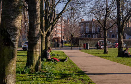 London, United Kingdom - APR 21, 2019 : Young people sit and relax on a green lawn in a park. Summer afternoon in the park. No focus, specifically.のeditorial素材