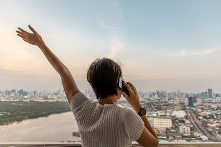 The back of young woman happy talking cell phone while standing on the balcony with against city view of bangkok. Copy space, Selective focus.の写真素材