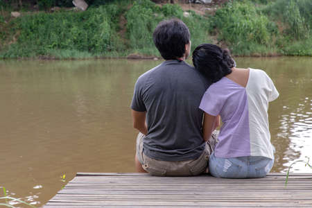 Rear view of young couple sitting in the border of a canal and watching river movement with together. Selective focus.の写真素材